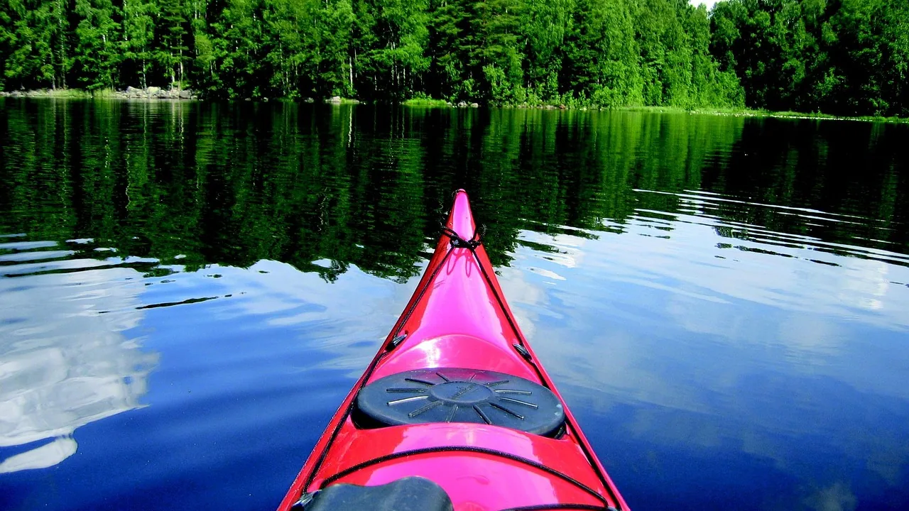 Kanot på en spegelblank skogssjö omgiven av grön barrskog en sommardag